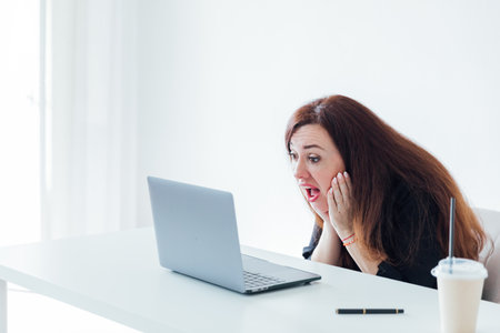 Brunette woman working with desk with laptop in white office onlineの写真素材