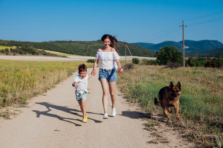 Mother with son and dog walking in rural field in summer by roadの写真素材