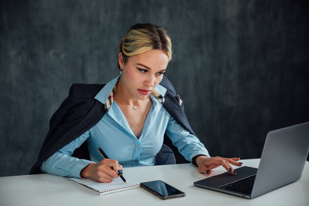 Blonde businesswoman working with laptop online at desk in officeの写真素材