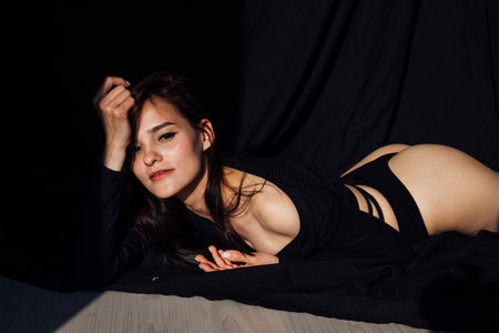 Slim brunette woman in black lingerie in bedroom on bed before bedの写真素材