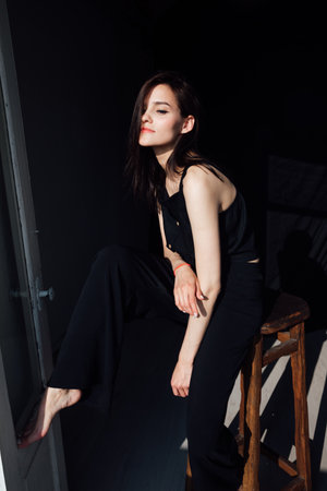 Slim fashionable woman in black clothes sitting on chair in roomの写真素材