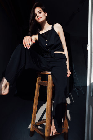 Slim fashionable woman in black clothes sitting on chair in roomの写真素材