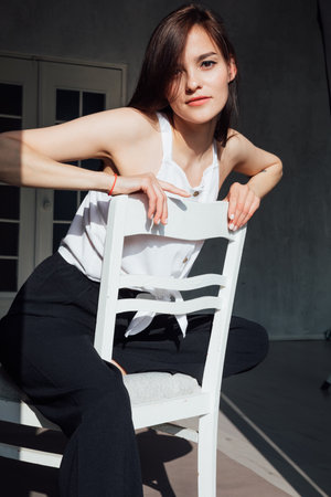 Slim fashionable woman in black clothes sitting on chair in roomの写真素材