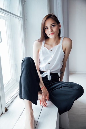 Slender woman sitting at the window in a white roomの写真素材