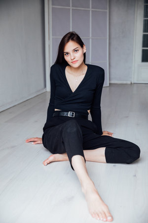 Slim woman in black clothes sitting on the floorの写真素材