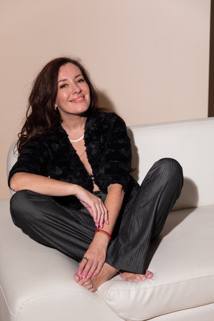 brunette woman in dark clothes sitting on white sofa in living room interiorの写真素材