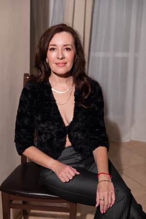 Brunette in dark clothes sitting on chair in roomの写真素材