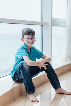 Boy in glasses for vision sitting by window in roomの写真素材
