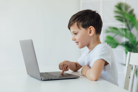 Boy working online at desk with study laptop at school
