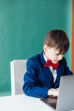Schoolboy in Jacket Sitting At Table With Educational Laptop Onlineの写真素材