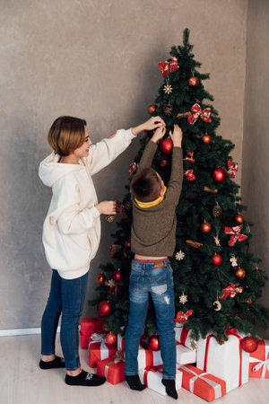 Mom and son decorating Christmas tree with gifts and toys for the new yearの写真素材