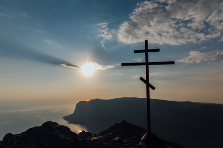 Silhouette of a Cross at Sunset with Mountains and Sea Backgroundの写真素材
