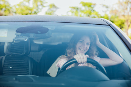 Excited young woman driving vehicle confidently, view from inside car interior at sunny day
