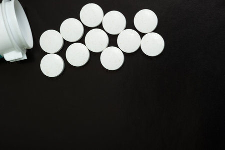 White tablets pour out of the jar on a black background. Vitamins, medications, top view.の写真素材