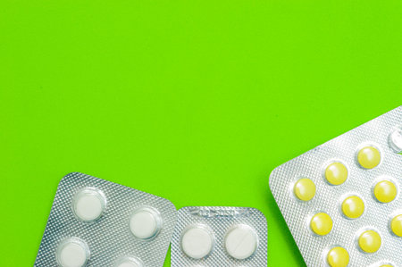 Three shiny packets of white and yellow tablets on a green background. Diseases, pharmaceuticals.