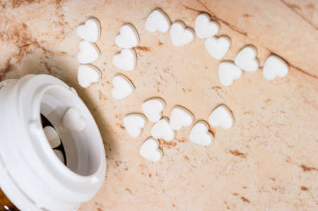 Pills in the shape of a heart on a pink marble background pour out of a jar of medicines.の写真素材
