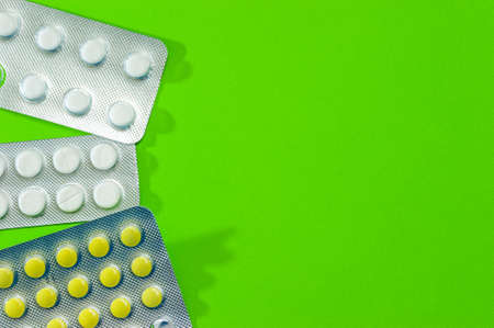 Three shiny packets of white and yellow tablets on a green background. Diseases, pharmaceuticals.の写真素材