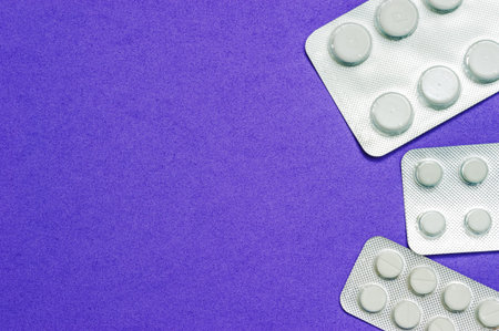 Three shiny packets of white pills on a blue background. Diseases, pharmaceuticals.