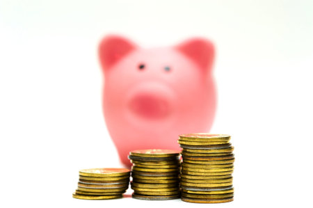 Three columns of yellow coins and a small pink piggy Bank in the background. The concept of lifes...