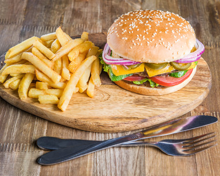 Fresh delicious Burger, bacon, cheese, tomato, French fries, onion and salad on a wooden table with...