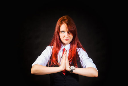 A pleading young redheaded woman a girl in a white blouse black vest and red tie on a black...