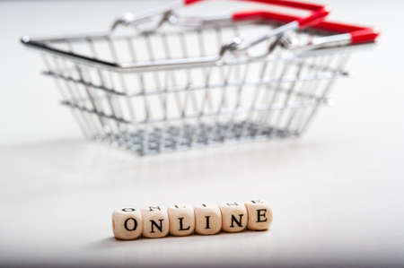 Online-an inscription made of wooden cubes on a white background and a metal shopping basket. Online sale.の写真素材
