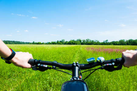 Handlebar from a Bicycle with mens hands, on the background of a summer meadow, riding a mountain bike on a path, in the countryside.の写真素材