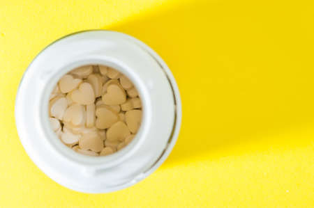 An open Jar with heart-shaped tablets, medications, dietary supplements on a yellow background.の写真素材