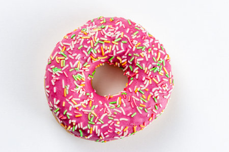 A pink doughnut decorated with multicolored splashes lies on a white table. The view from the top