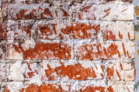 Old worn red brick wall with knocked down plaster, chipped, scratched with plaster, close-up,...