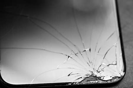 The cell phone screen is shattered. Web of cracks in all directions, black and white photoの写真素材