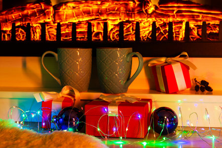 Two Christmas cups of coffee or tea by the fireplace surrounded by giftsの写真素材