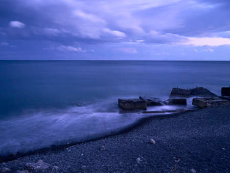 seascape after sunset, cloudy sky, shore with small pebbles, concrete blocks lie on the shore, the horizon line is clearly visible, calm and tranquilityの写真素材