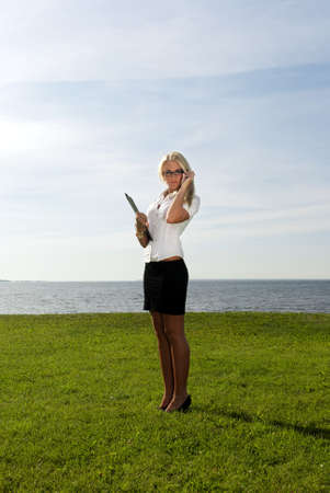 girl in glasses standing with a folder on the background of the sea, sky and grassの写真素材