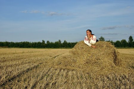 girl in traditional Russian costume lying on a haystack, space for textの写真素材