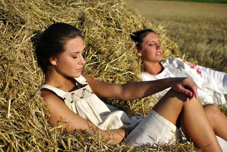 two girls in traditional Russian costume resting on a haystackの写真素材