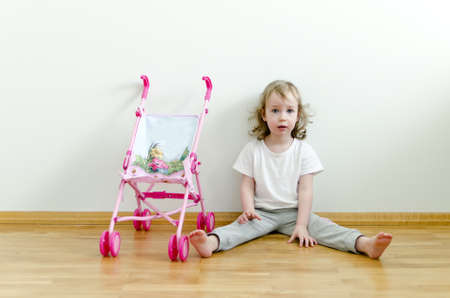 Little cute girl sitting on the floor next to the toy strollerの写真素材
