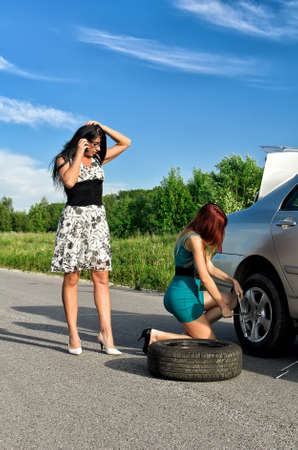 Two women are changing a tire on a roadの写真素材