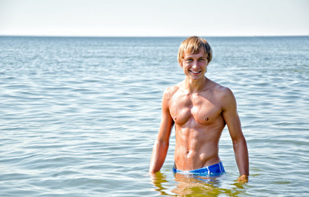 Semi nude handsome smiling man standing in the seaの写真素材