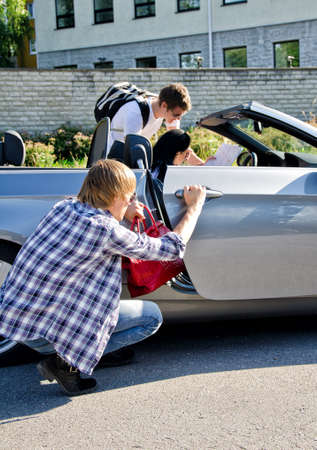 Male thief stealing handbag from the car while his accomplice distracts female driverの写真素材