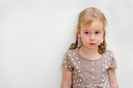 Portrait of sad little girl standing against the wall  Space for text