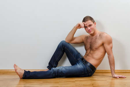Handsome guy in jeans with bare torso sitting on the floor near the wallの写真素材
