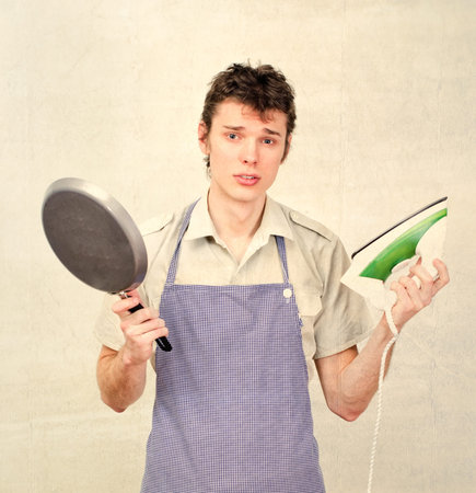 Young man wearing apron and holding pan and ironの写真素材