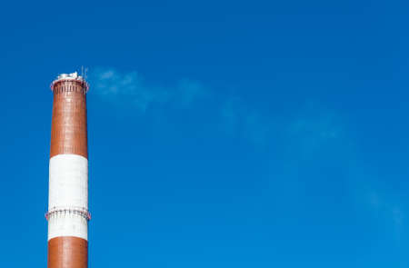 Industrial chimney with smoke over blue skyの写真素材