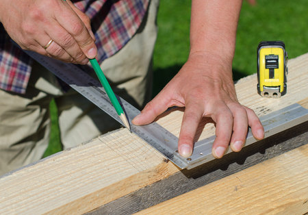 Male hands measuring and marking wooden plank outdoors