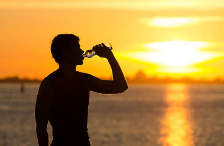Man drinking bottle of water on the beach at sunriseの写真素材