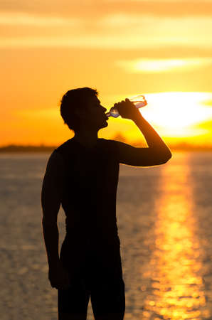 Man drinking bottle of water on the beach at sunriseの写真素材