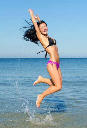 Happy woman jumping in the water at the beachの写真素材