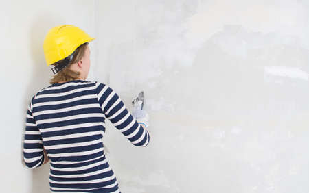 Female plasterer repairs wall with spackling paste  Space for your text の写真素材