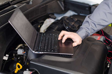 Mechanic with laptop diagnoses car in workshop の写真素材
